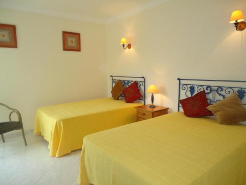 a bedroom with two beds with yellow sheets and red pillows at Vilas do Mar in Carvoeiro