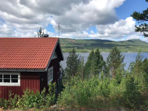 a red house with a red roof next to a lake at Chalet in Torsby Municipality Middle with Sauna in Gunsjögården