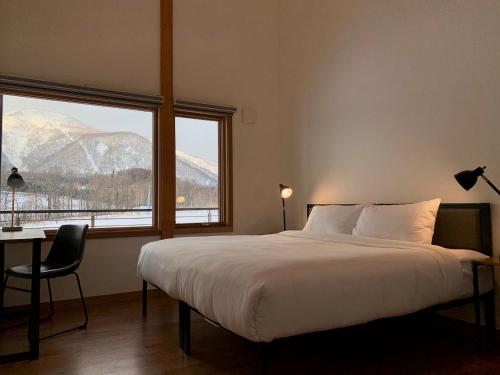 新雪谷的住宿－Hakobune Niseko - Chalets & Apartments，一间卧室配有一张床、一张书桌和两个窗户。