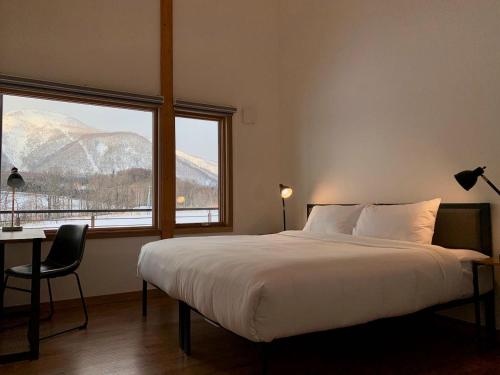 a bedroom with a bed and a desk and two windows at Hakobune Niseko - 8-room Chalets & 2-room Apartments in Niseko