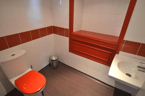 La salle de bains est pourvue de toilettes rouges et d'un lavabo. dans l'établissement Hôtel Restaurant La Régence, à Lourdes