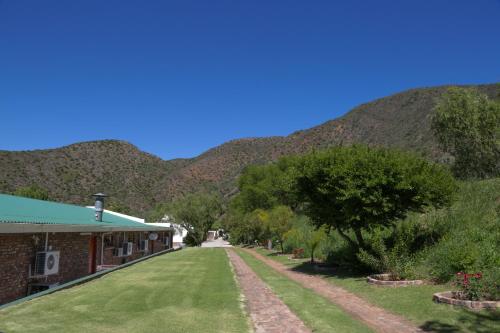 a building with a green lawn in front of a mountain at De Oude Meul Country Lodge & Restaurant in Oudtshoorn