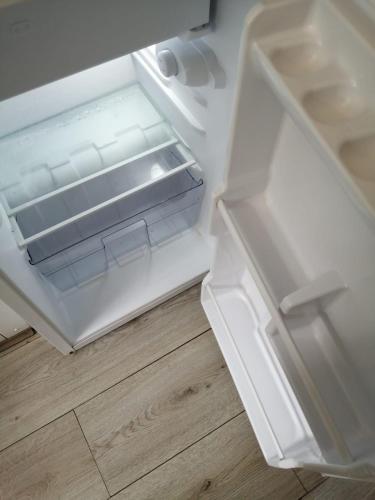 an empty refrigerator with its door open on a wooden floor at White Lodge in Caernarfon