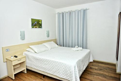 a small bedroom with a white bed and a night stand at De Rose Centro Hotel in Torres