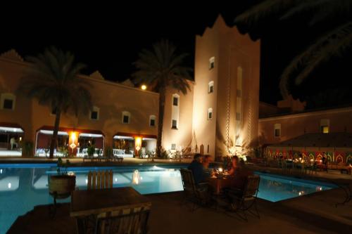 a couple sitting at a table by a pool at night at Hôtel Le Tinsouline in Zagora