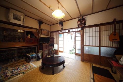 Sala de estar con mesa y puerta con guitarra en Buddha Guest House en Tanabe