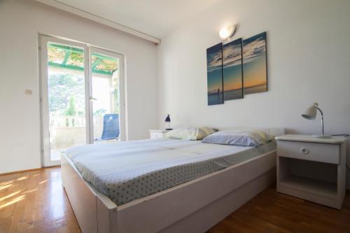 a white bedroom with a large bed and a window at Apartments Radić in Bol