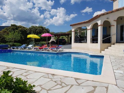 a swimming pool with chairs and umbrellas next to a house at Stylish villa with private pool in Félines-Minervois