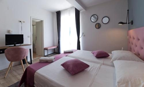 a bedroom with two beds with purple pillows and a desk at Hotel Perla in Dubrovnik