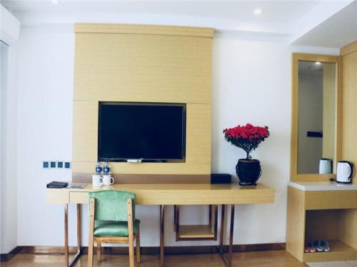 a desk with a television and a vase of flowers at GreenTree Inn HuaiAn Area for development Shenzhen East Road Express Hotel in Huai'an