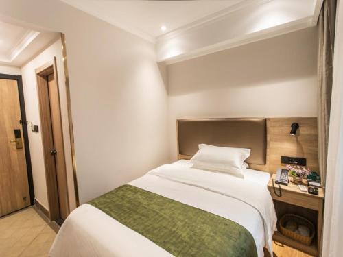 a bedroom with a large white bed with a green blanket at GreenTree Inn Suzhou Humble Administrator's Garden Railway Station South Square in Suzhou