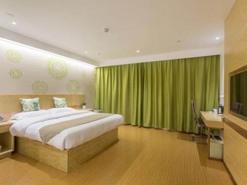 a bedroom with a bed and a desk and green curtains at GreenTree Inn Xuzhou Ou Shasha Building Materials City Express Hotel in Xuzhou