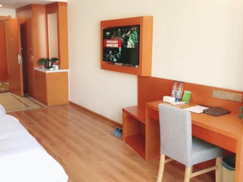 a room with a desk and a bed and a television at Vatica Fuyang Linquan County Tenghui International City Hotel in Fuyang