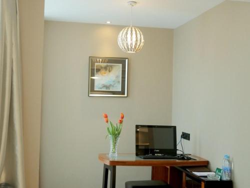 a desk with a computer and a vase of flowers on it at GreenTree Alliance AnHui HeFei MengCheng North Road JiQiao Road Hotel in Hefei
