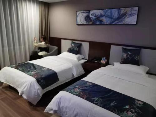 una habitación de hotel con 2 camas y una mujer en la ventana en Shell Fuyang City South Bus Station Hotel, en Fuyang