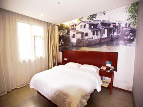 a bedroom with a large bed with a painting on the wall at GreenTree Inn JiangSu SuZhou International Film City South JinShan Road Express Hotel in Suzhou
