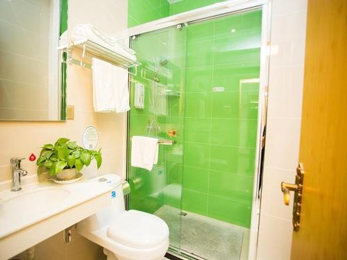 a green bathroom with a toilet and a glass shower at GreenTree Inn Tangshan Qianxi Bus Terminal Express Hotel in Qian'an