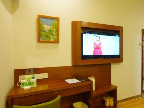a room with a tv on a wall with a desk at Vatica AnHui Fuyang Linquan South Jiefang Hotel. in Linquan
