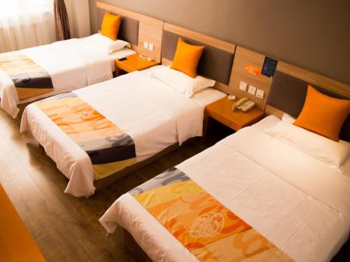 a hotel room with three beds with orange pillows at Shell Tangshan Caofeidian District Xinghai Mingdu Plaza Hotel in Tangshan