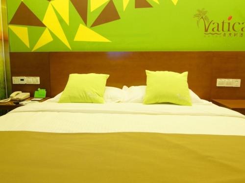 a large bed with yellow pillows and a green wall at Vatica AnHui Fuyang Linquan South Jiefang Hotel. in Linquan