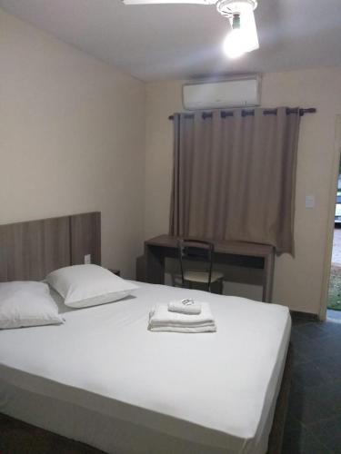 a bedroom with a white bed with a desk and a window at Hotel Pousada Jaguariuna in Jaguariúna