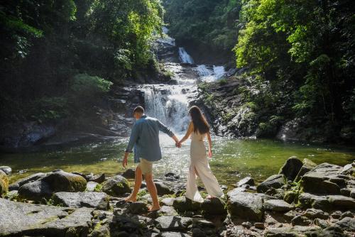 a man and woman walking across rocks in front of a waterfall at JW Marriott Phuket Resort and Spa in Mai Khao Beach