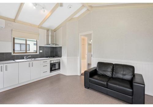 a living room with a black leather couch in a kitchen at Discovery Parks - Warrnambool in Warrnambool