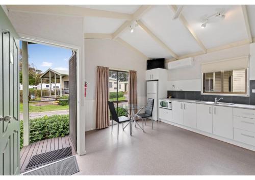 a kitchen with white cabinets and a table with chairs at Discovery Parks - Warrnambool in Warrnambool