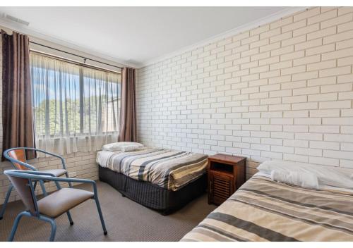 a bedroom with two beds and a chair and a window at Discovery Parks - Warrnambool in Warrnambool