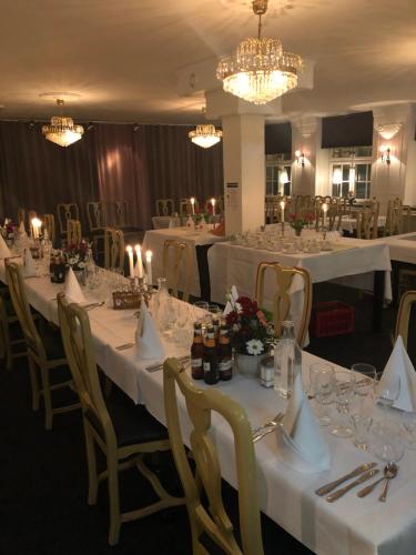 uma sala de jantar com mesas e cadeiras brancas e lustres em Värdshuset Hwitan em Falkenberg