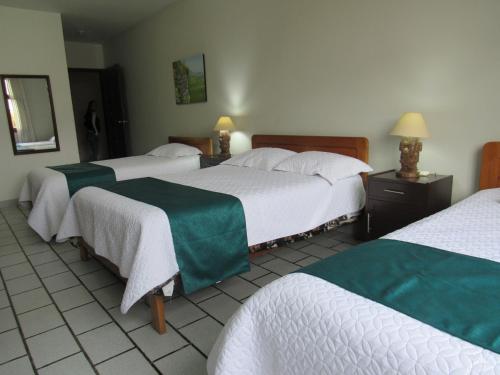 Las Orquídeas Hotel 3 estrellas في شاشابوياس: غرفة في فندق بثلاث اسرة شراشف خضراء وبيضاء