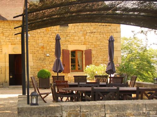 a wooden table with chairs and umbrellas in front of a building at Chambres d'hôtes avec Piscine la Rossillonie in Beynac-et-Cazenac