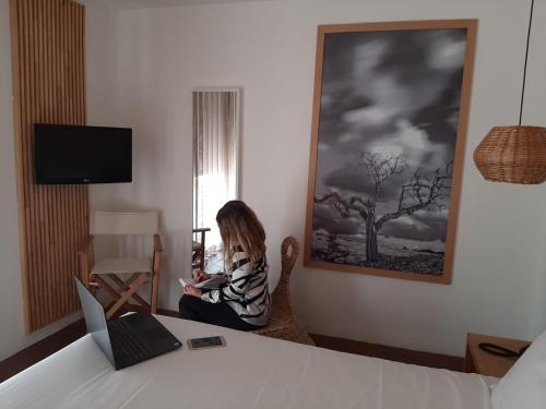a woman sitting on a bed in front of a painting at ECORKHOTEL Evora in Évora