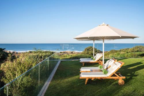 two chairs and an umbrella on a lawn with the ocean at Palacio de Sancti Petri, a Gran Meliá - The Leading Hotels of the World in Chiclana de la Frontera