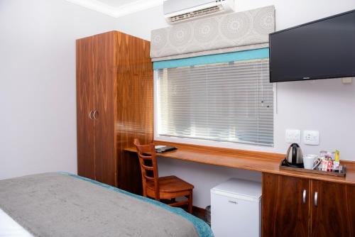 a bedroom with a desk and a bed and a window at Palm Park Hotel in Ellisras