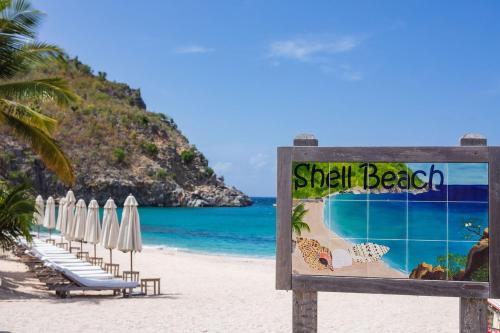 a sign on a beach with chairs and umbrellas at Hôtel Barrière Le Carl Gustaf St Barth in Gustavia