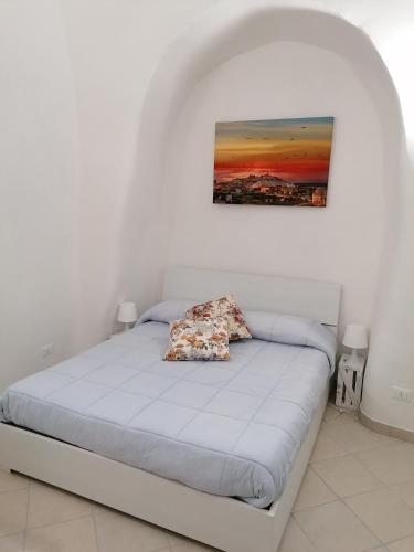 uma cama num quarto branco com uma fotografia na parede em Casetta Carlotta em Ostuni