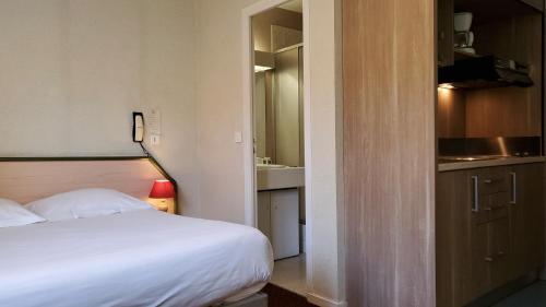 a bedroom with a white bed and a kitchen at Résidence Wilson in Le Mont-Dore