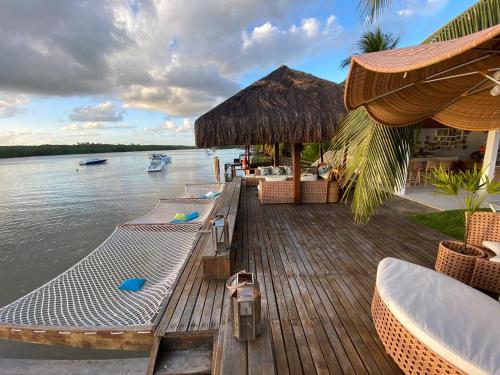 une terrasse en bois avec des chaises et un bateau sur l'eau dans l'établissement Casa praia Porto de Galinhas Toquinho, à Ipojuca