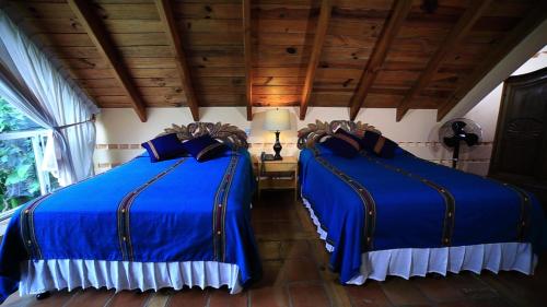 two blue beds in a room with wooden ceilings at Hotel San Buenaventura de Atitlán in Panajachel