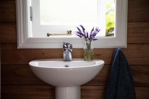 a bathroom sink with a vase of purple flowers on it at Beach Folly - Whitianga in Whitianga