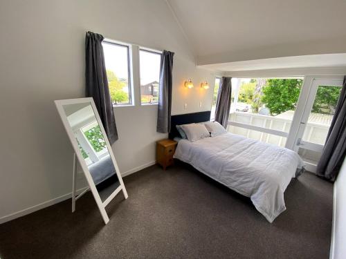 a bedroom with a bed and a mirror and windows at Chamberlain House - 3 bedroom house by Manly beach in Auckland