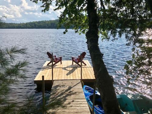a dock with two chairs and a boat on a lake at Chalet "Ici et maintenant, sur le lac" in Sainte-Marguerite