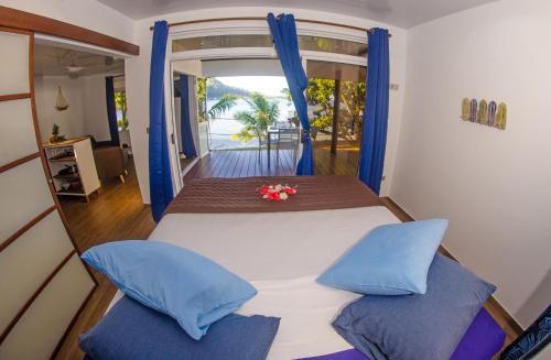 a bedroom with a bed with blue pillows and a window at Le Neliza Beach Lodge Raiatea in Opoa