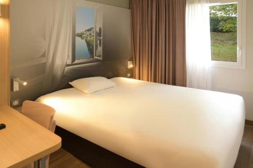 a large white bed in a room with a window at B&B HOTEL Angoulême in Le Gond-Pontouvre