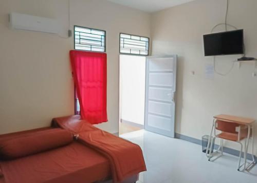 una camera con letto rosso, scrivania e TV di Homestay Verisha Mitra RedDoorz a Singkawang