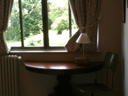 a table with a lamp in front of a window at La Foutelaie in Clefs