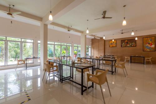 a dining room with tables and chairs and windows at KSTDC Hotel Mayura Kauvery KRS in Hosa Kannambādi