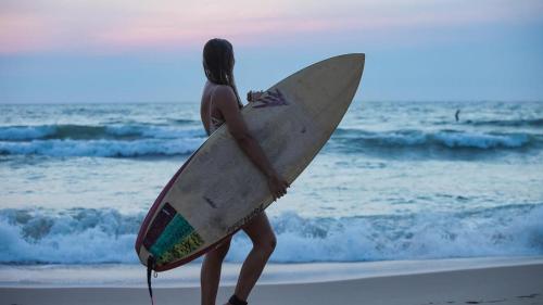 a woman walking on the beach holding a surfboard at Les Pieds dans l'Eau in Lacanau-Océan