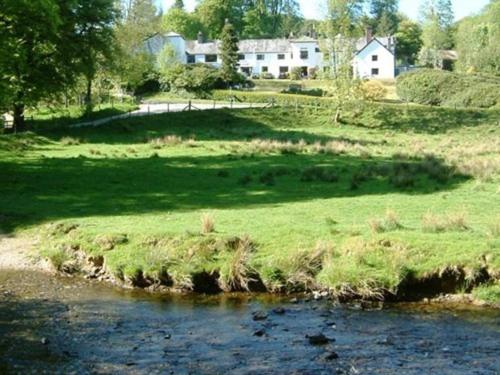 a field of grass next to a river with a house at Simonsbath House Hotel in Simonsbath